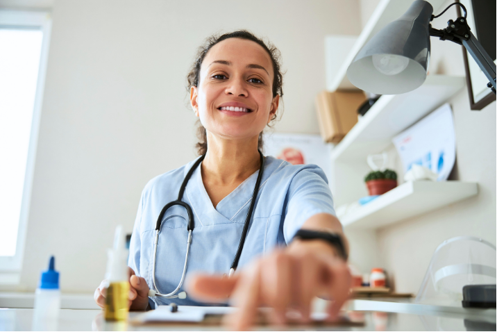 A physician smiles down toward the camera from behind her desk.