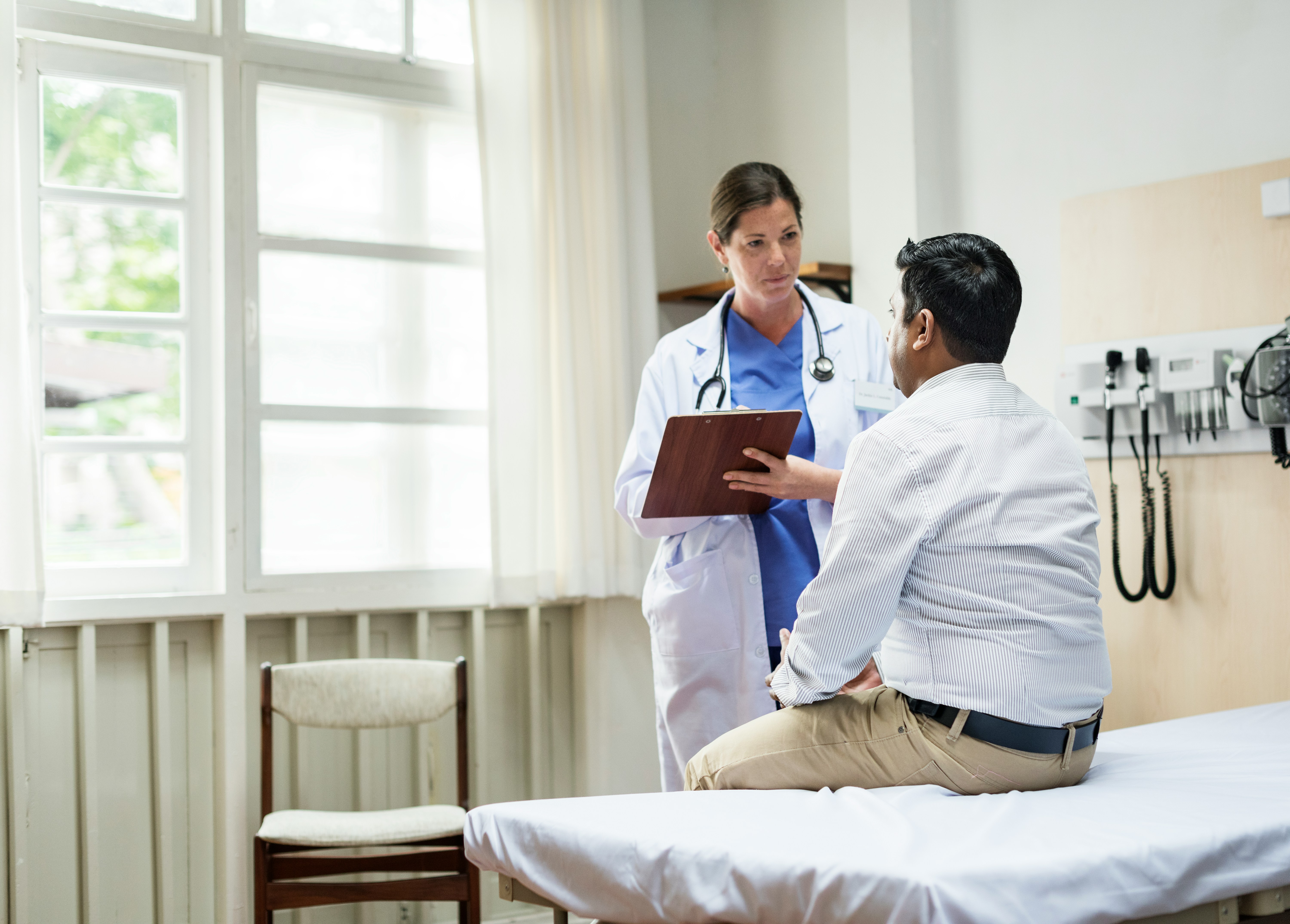 Une médecin, tenant un porte-bloc, regarde sa patiente assise sur un lit d’hôpital.