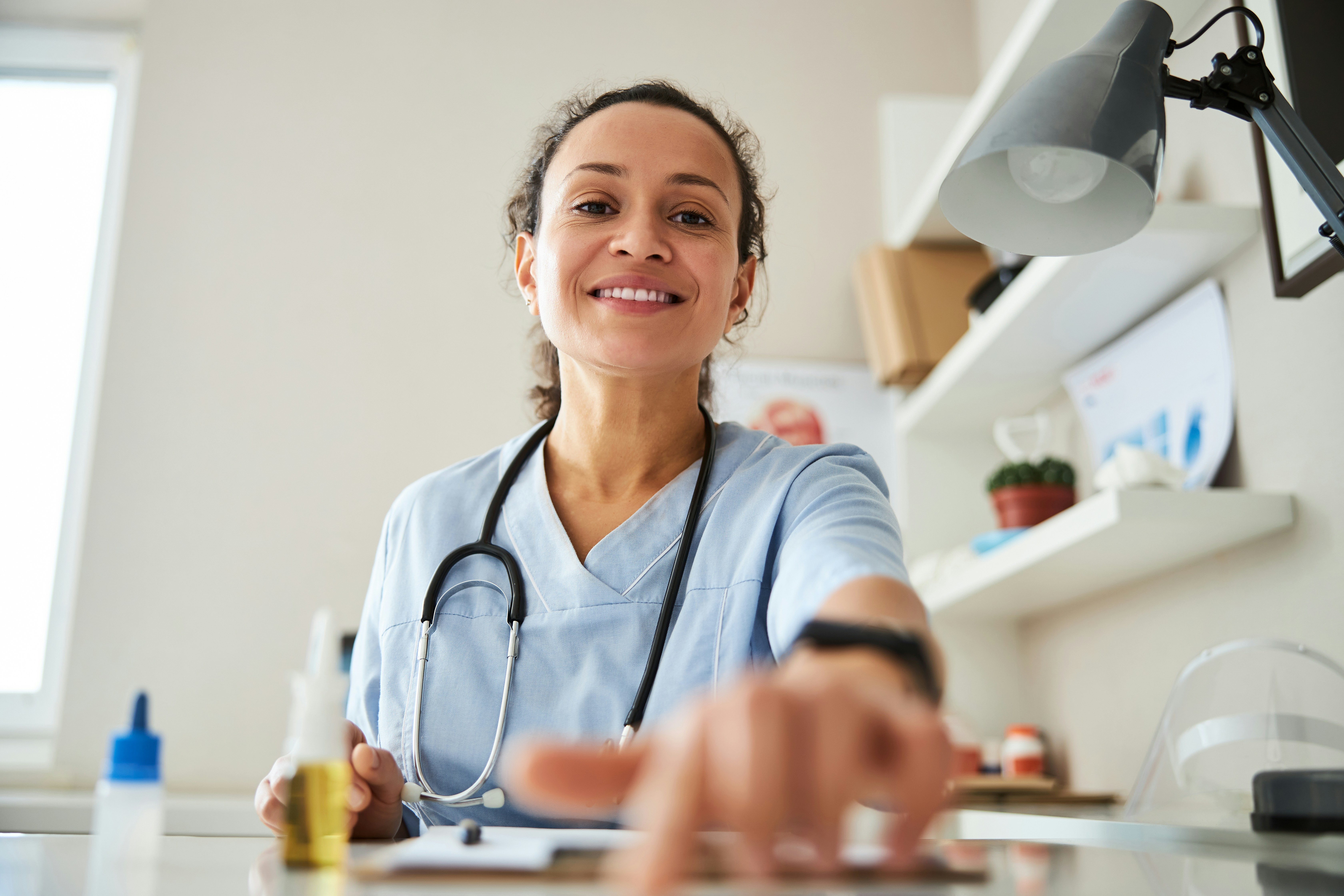 A physician smiles down toward the camera from behind her desk.