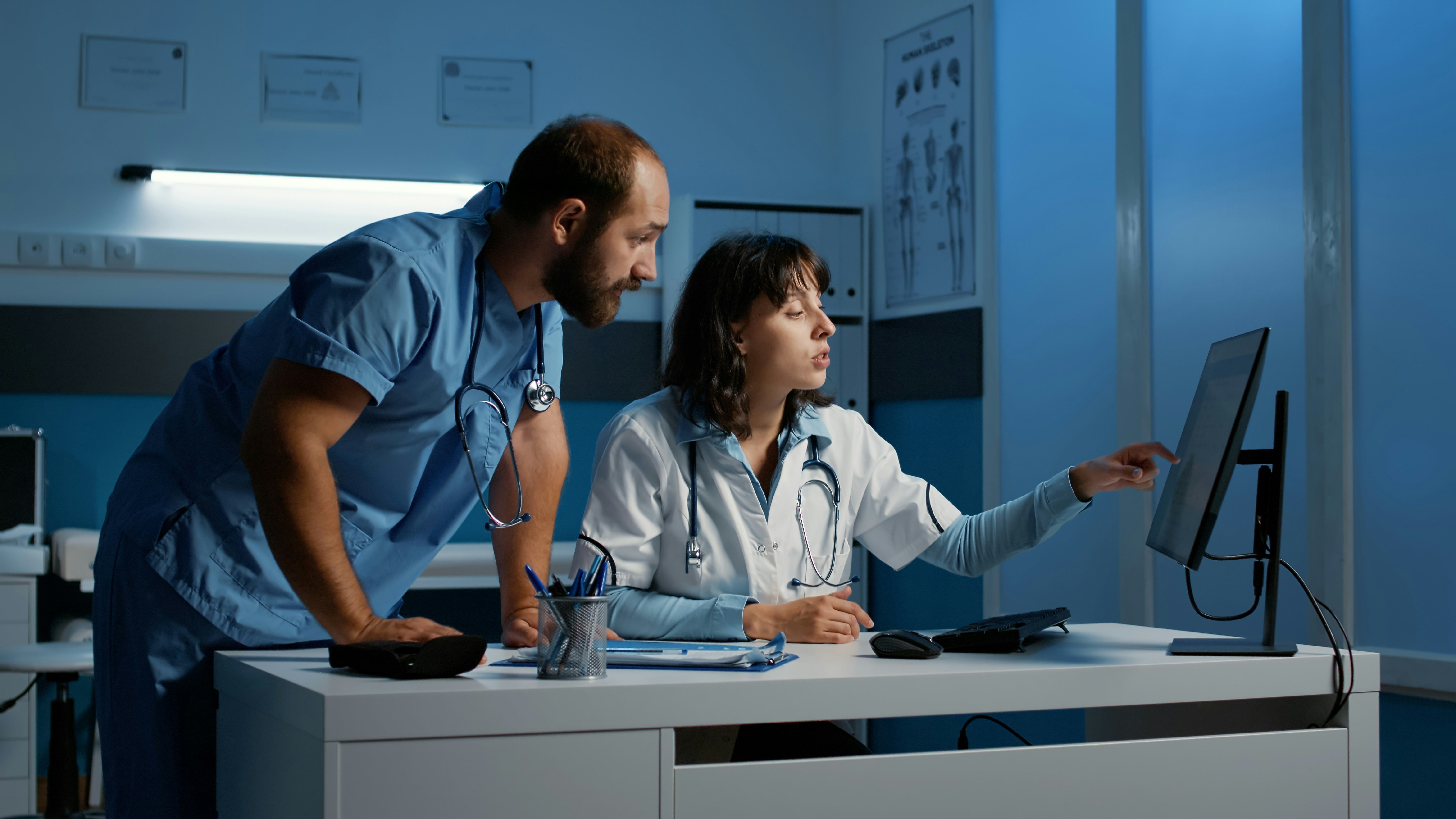 Un médecin pointe un écran d’ordinateur pendant qu’une autre médecin regarde par-dessus son épaule.
